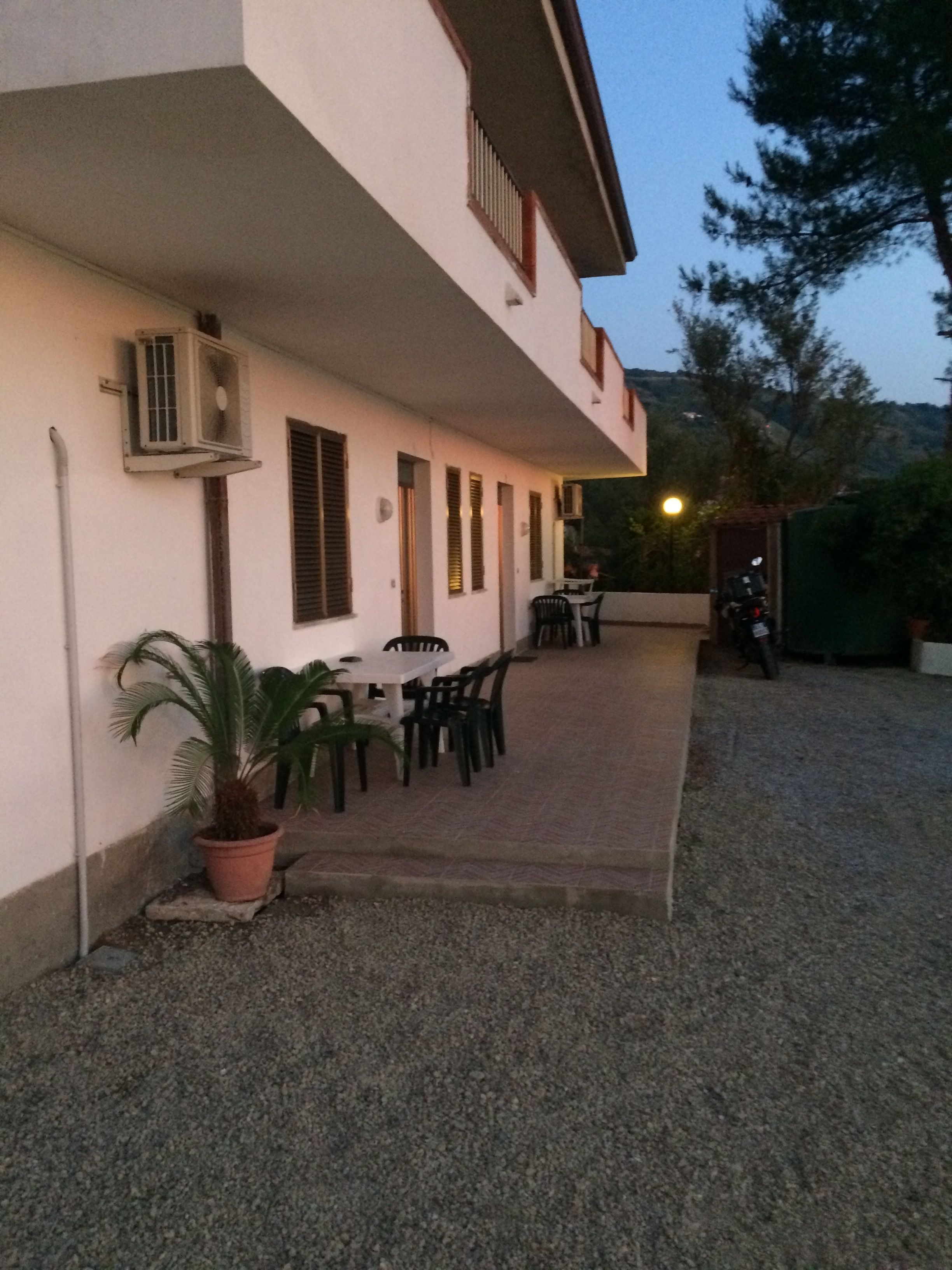 A building with a covered patio area, outdoor seating, and a motorcycle parked nearby.