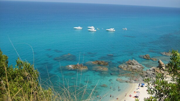 Une vue sur la côte, avec des bateaux, une eau turquoise et limpide, un rivage rocheux et une plage de sable.