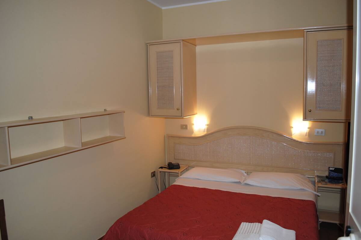 A hotel room with a bed, bedside tables, a mirror, and a shelf.
