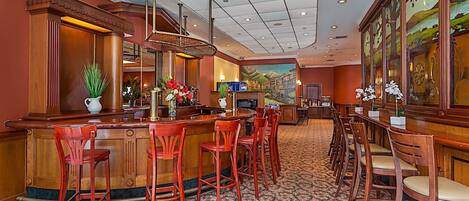 A bar area with wooden bar counters, red chairs, and a patterned carpet.