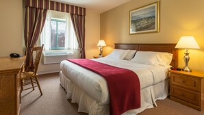 A hotel room with a large bed, two bedside lamps, a wooden nightstand, a desk with a chair, and a window with curtains. - Chelsea Savoy Hotel (New York)