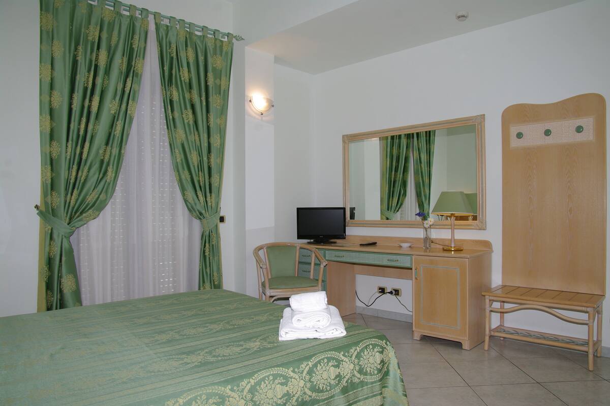 A hotel room with a bed, a desk, a chair, a television, and a mirror.