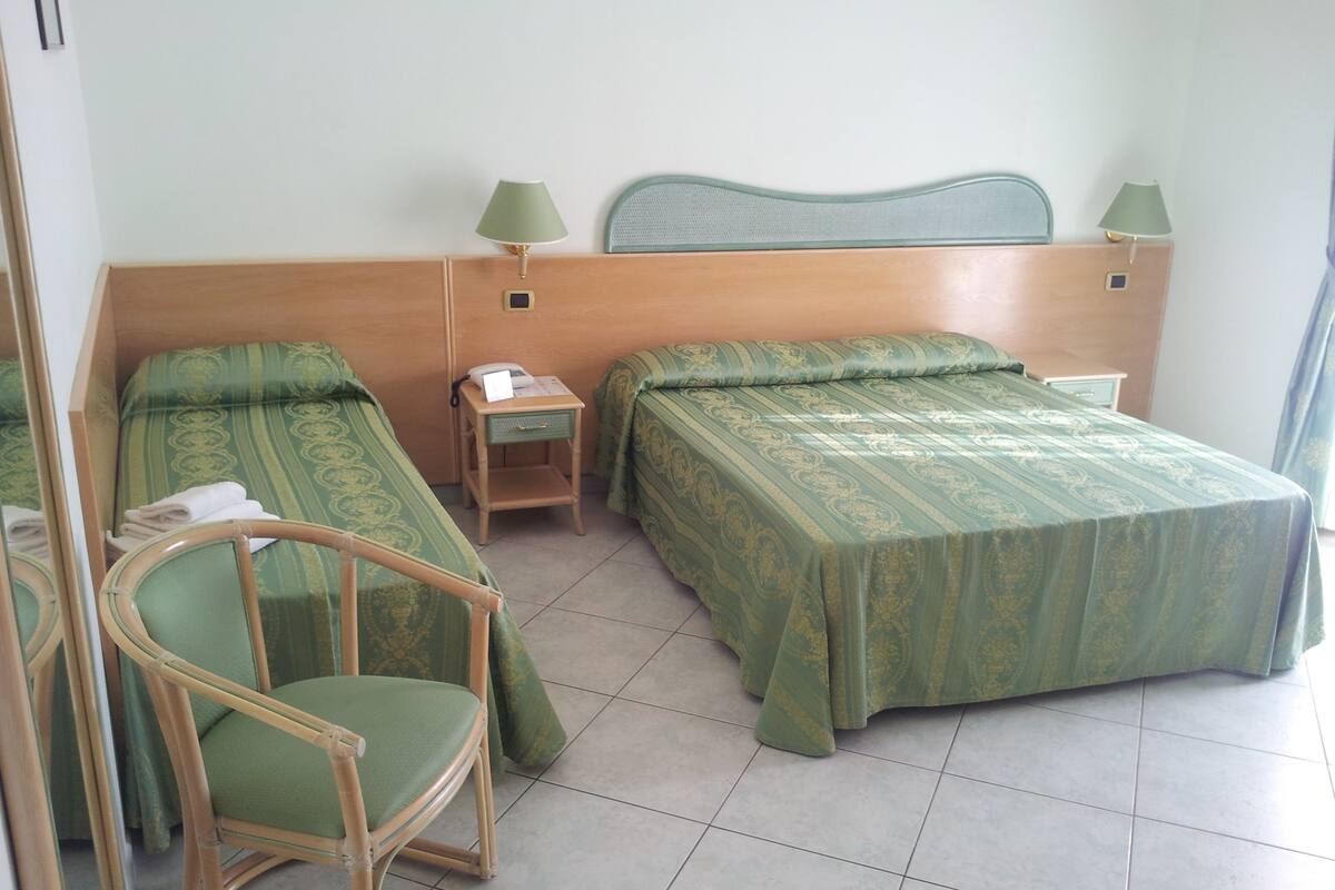 A hotel room with two single beds, a wooden headboard, a small bedside table with a lamp, and a chair.