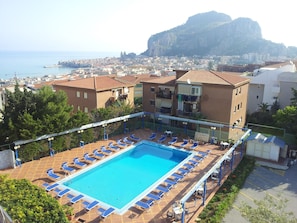 Une piscine sur le toit, dotée de chaises longues, offrant une vue sur la ville et avec une montagne en arrière-plan.
