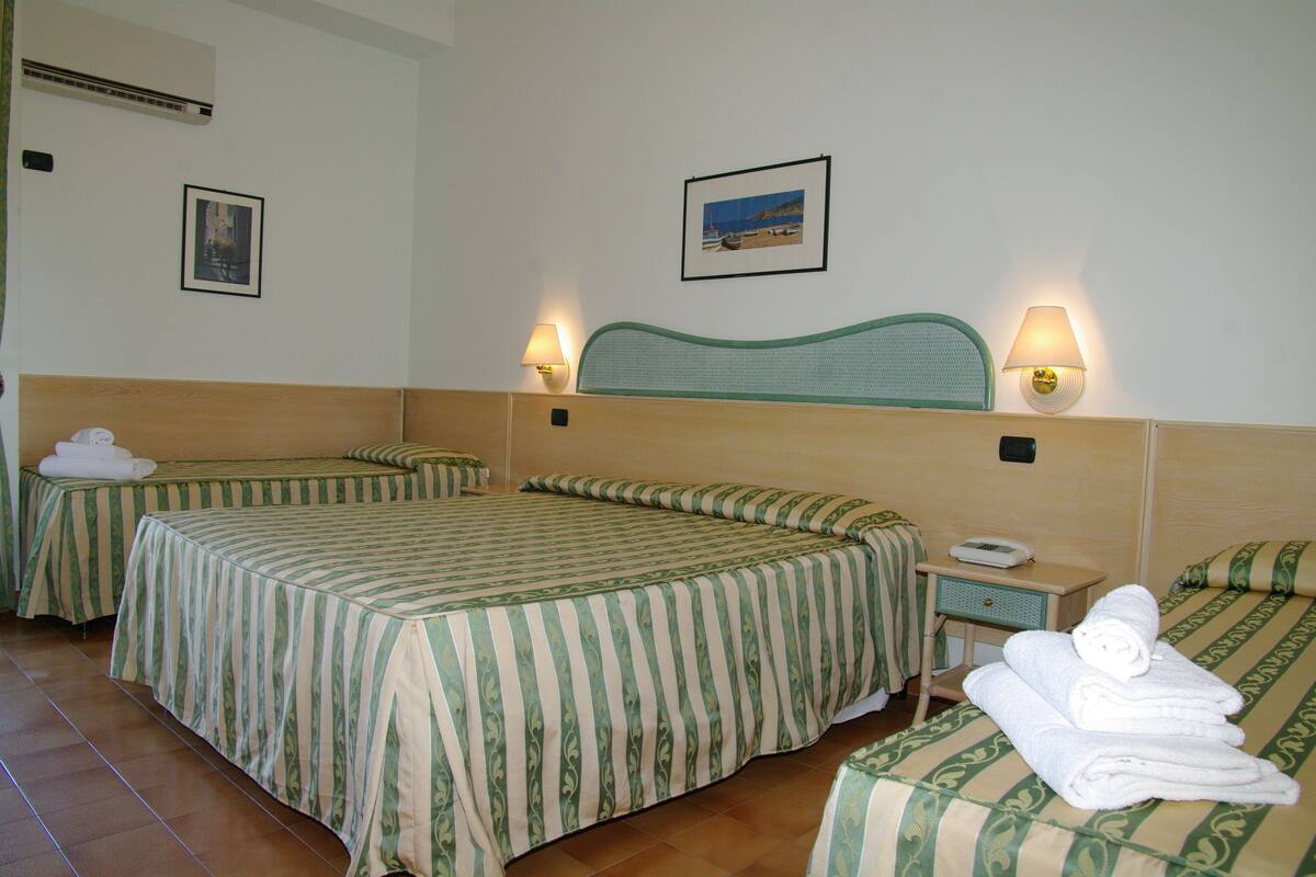 A hotel room with two beds, each with striped bedding, a headboard, bedside lamps, and a small bedside table with a phone.