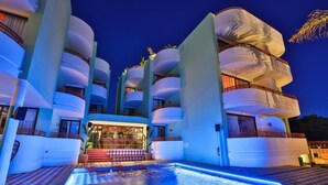 Un hôtel moderne doté de nombreux balcons, d’une piscine et d’une entrée bien éclairée.