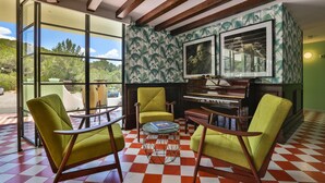 Une pièce dotée de grandes fenêtres, d’un piano, de chaises vertes et d’un sol à carreaux.