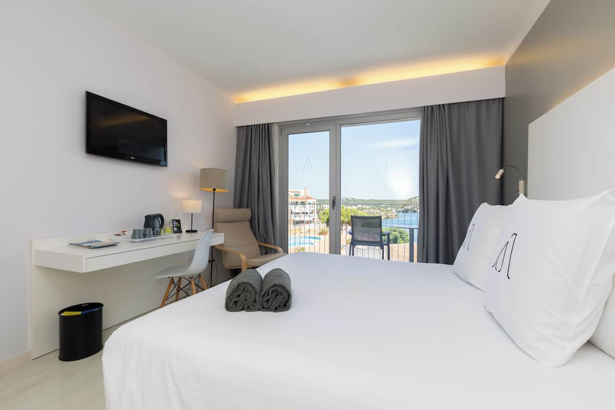 Habitación de hotel con cama, escritorio, silla, televisión y vista al exterior.