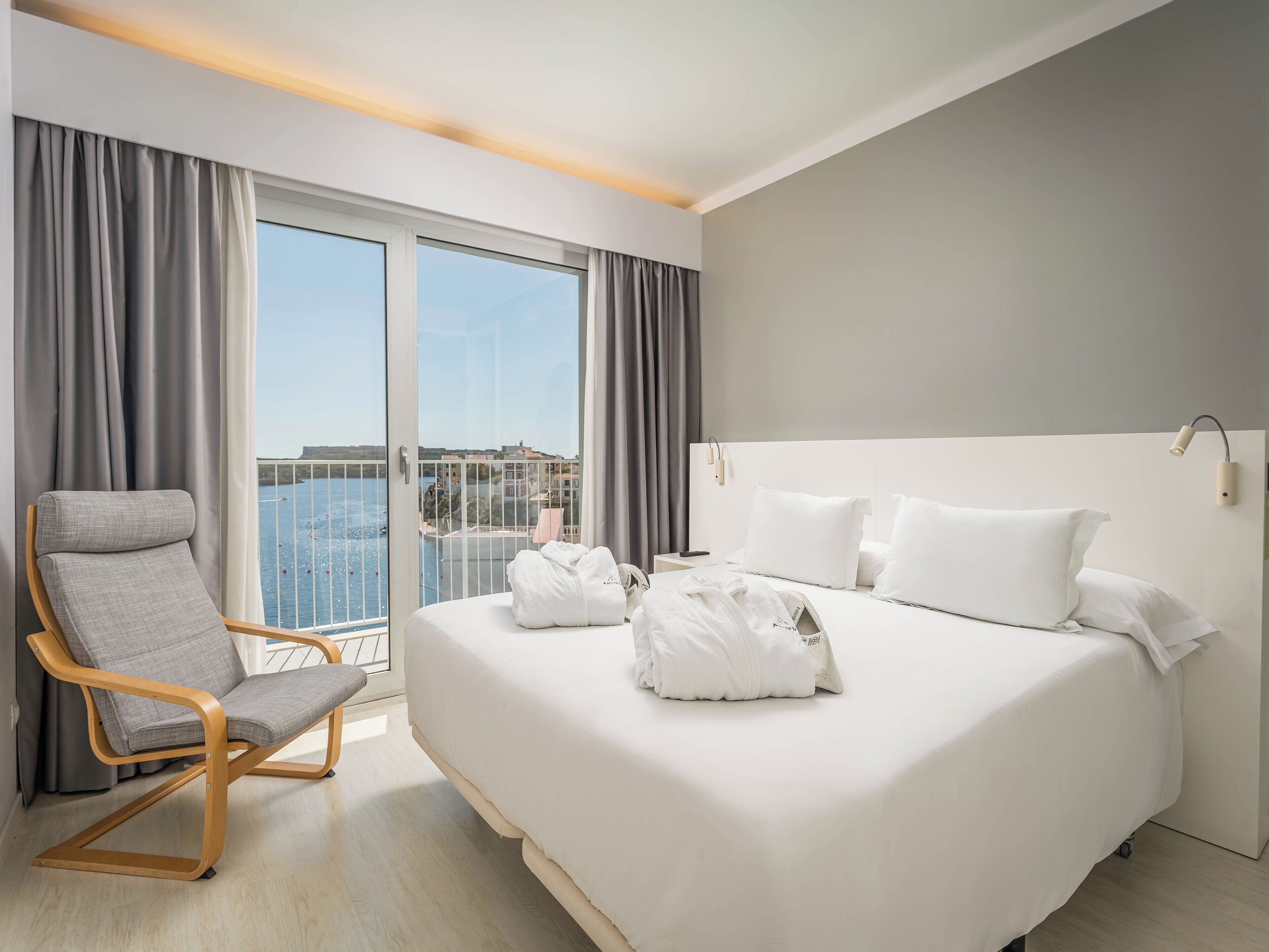 A hotel room with a large bed, a chair, and a view of the sea.