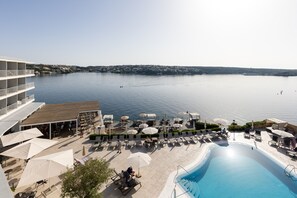 A resort with a swimming pool, lounge chairs, umbrellas, and a view of the water.