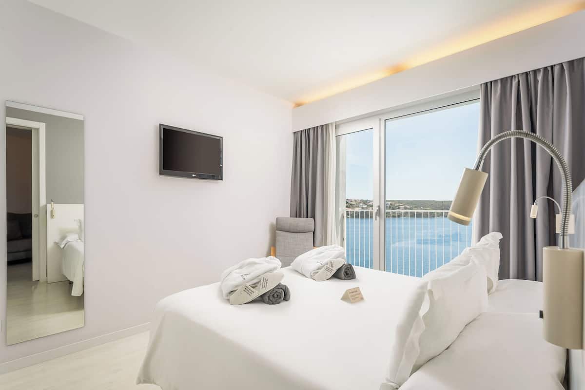 Una habitación de hotel con cama, televisión, balcón con vistas y lámpara.