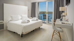 A hotel room with a bed, a desk, a chair, a TV, and a balcony with a view of the sea. - ARTIEM Carlos - Adults Only Hotel (Es Castell)