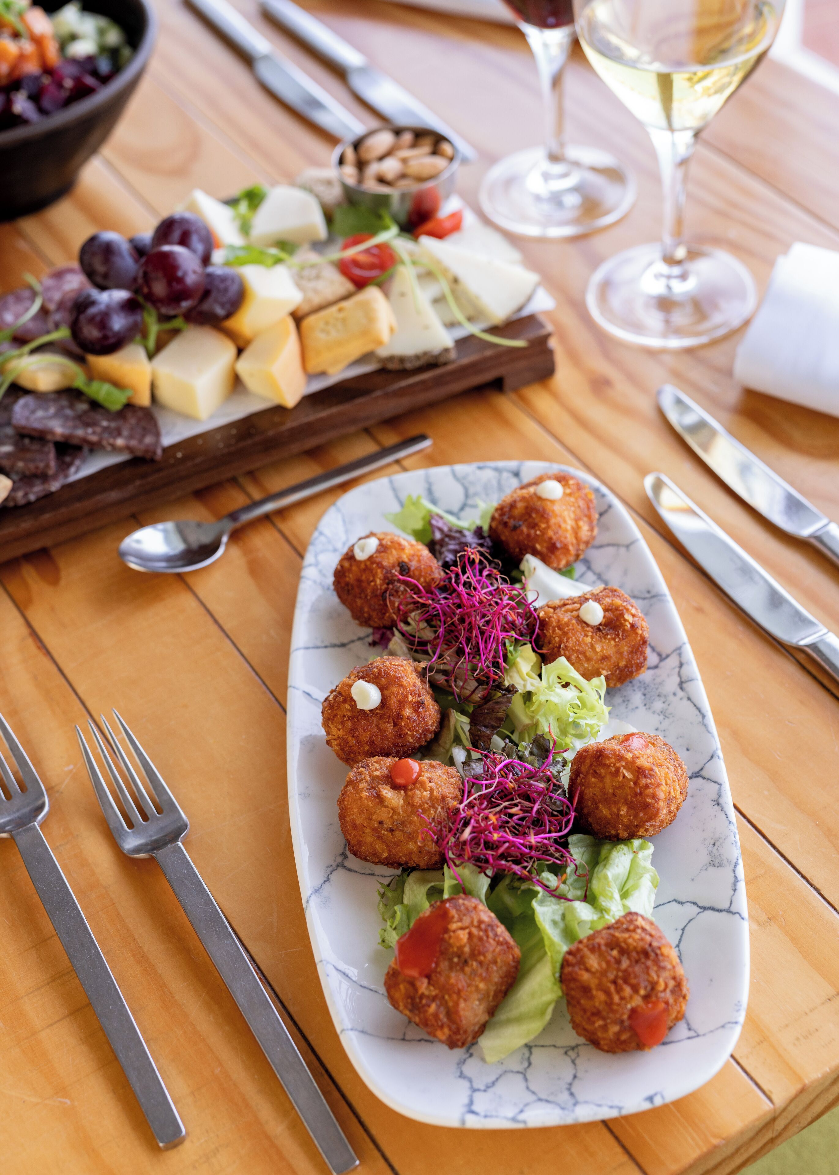 A dining table with a plate of food, cutlery, and a glass of white wine.