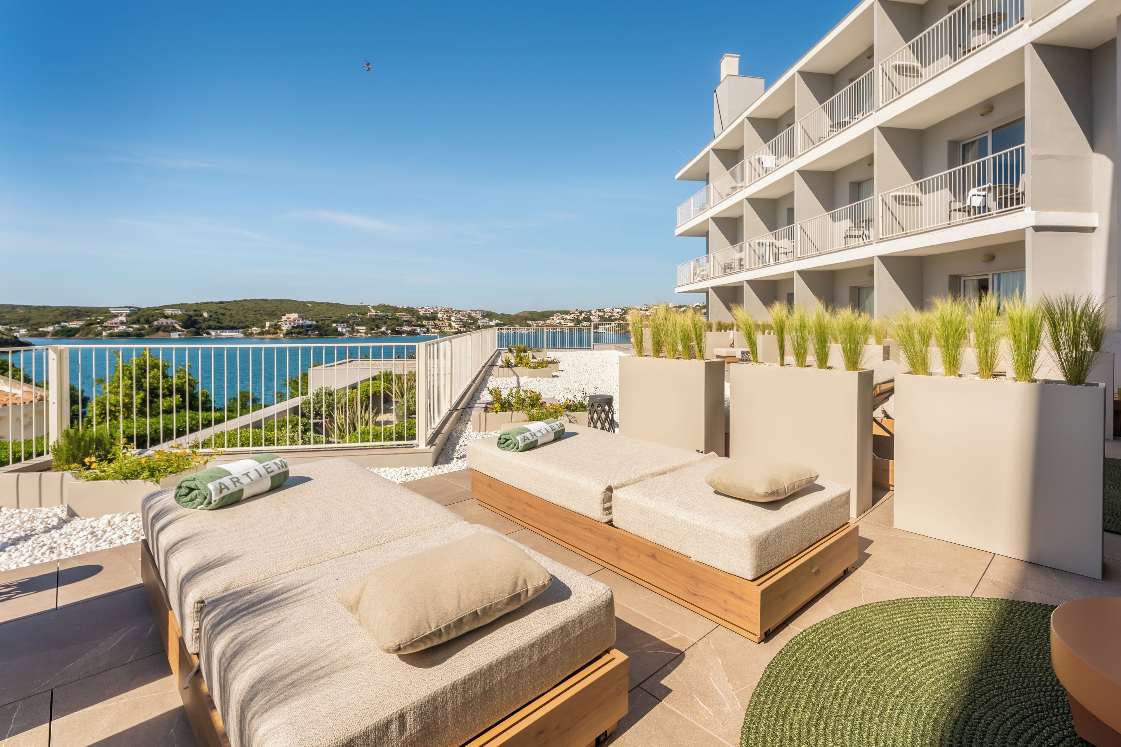 A balcony with a view of the sea, a pool, and a building with multiple balconies.