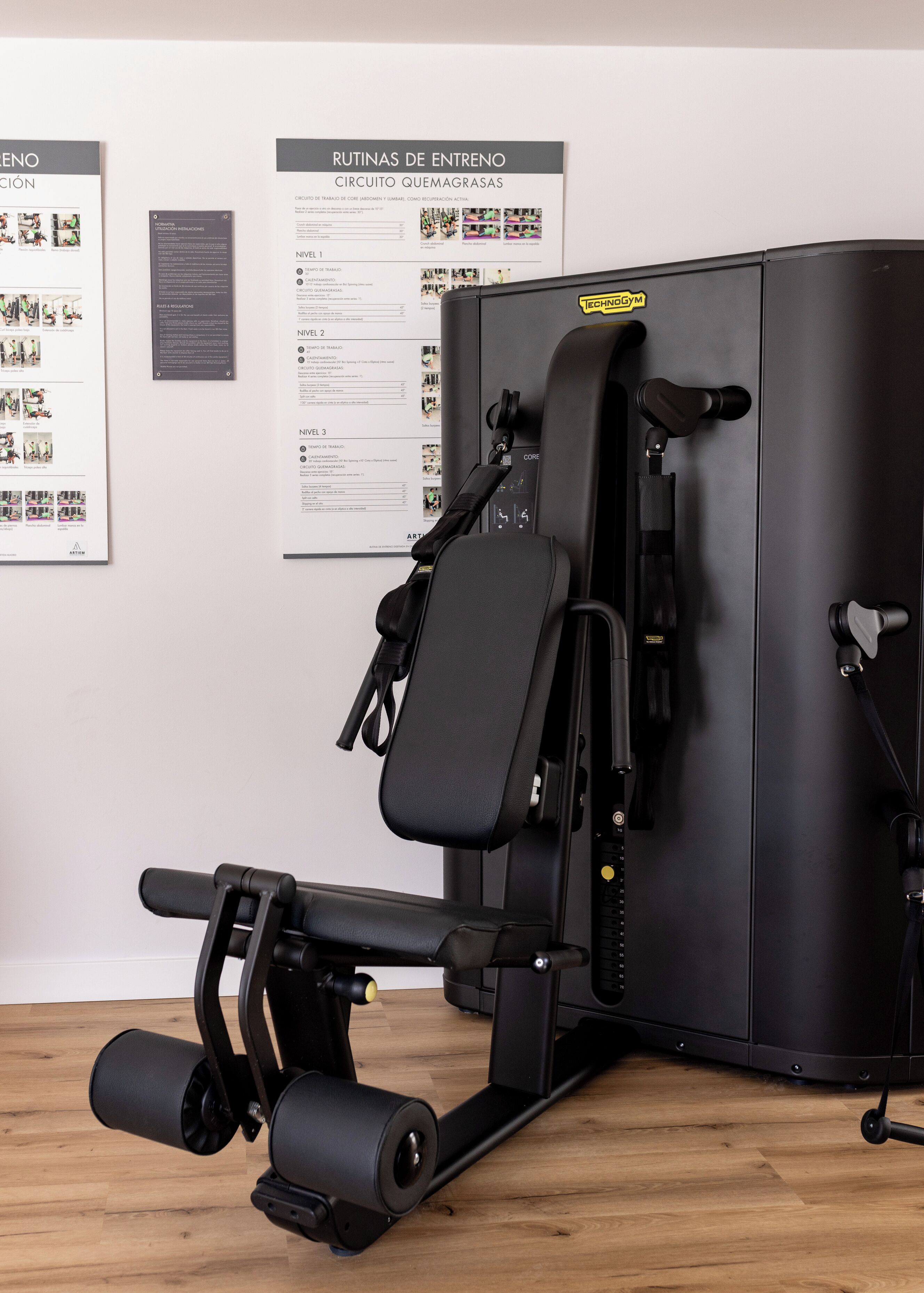 Un gimnasio con una máquina de ejercicio negra, suelo de madera y carteles informativos en la pared.