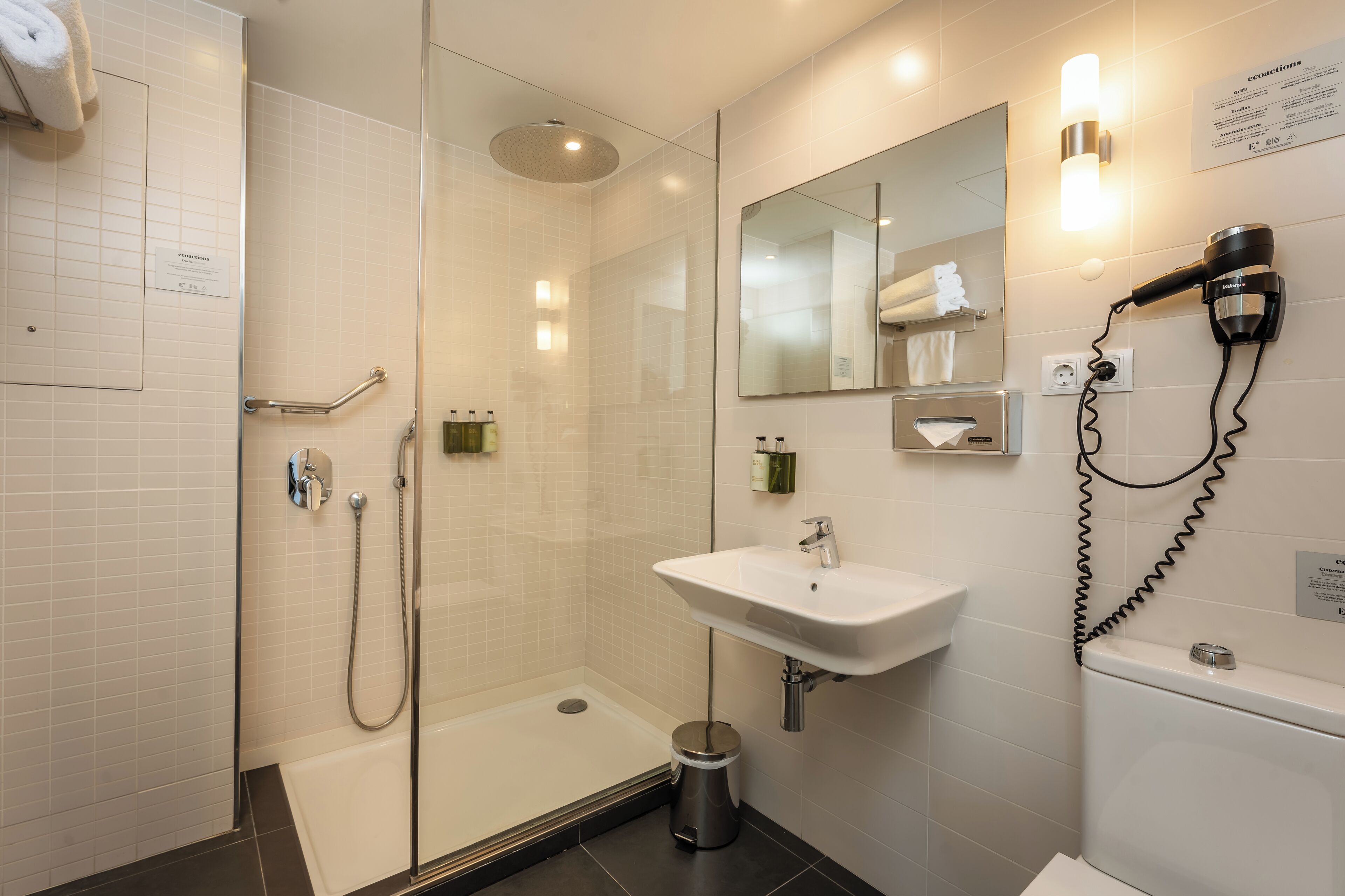Un baño moderno con cabina de ducha de vidrio, un lavabo, un secador de pelo y un inodoro.