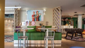 Een gezellige zithoek met een groene bank, twee metalen stoelen, een klein rond tafeltje en een tafelvoetbaltafel.