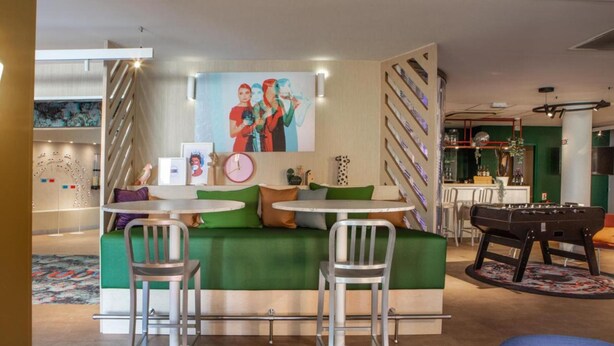 Un rincón de sala acogedor con un sofá verde, dos sillas de metal, una mesita redonda y una mesa de futbolín.