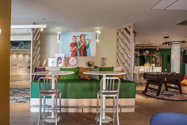 Ein gemütlicher Lounge-Bereich mit einem grünen Sofa, zwei Metallstühlen, einem kleinen runden Tisch und einem Kicker.