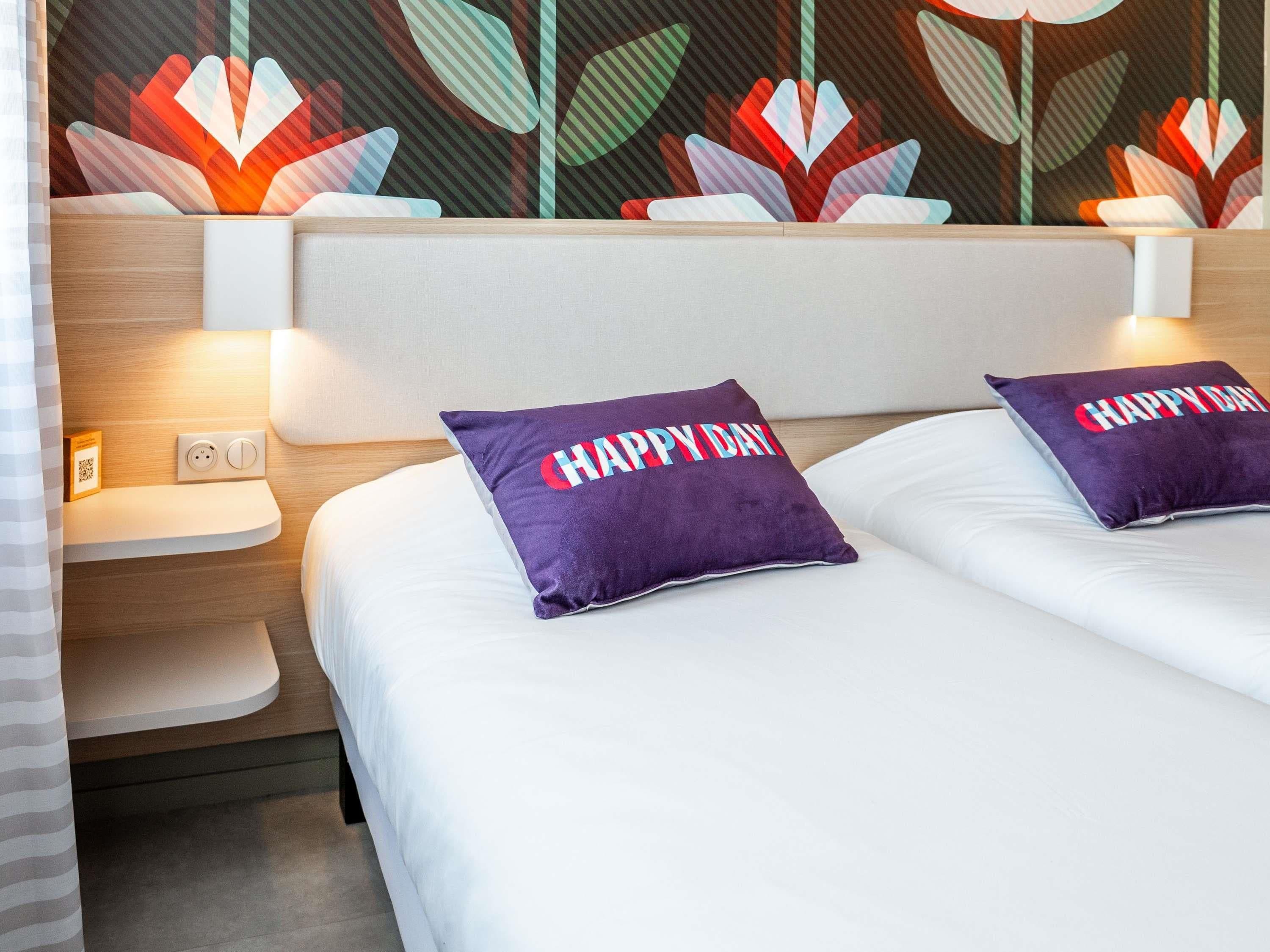 Una habitación de hotel con dos camas, cada una con un almohadón que dice 'HAPPY DAY'.