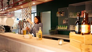 Een bar met een toonbank, iemand die een drankje schenkt en planken met flessen en glazen.