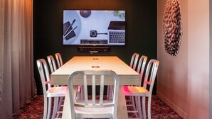 Una sala de conferencias con una larga mesa, seis sillas, una pantalla grande y una lámpara en el techo.