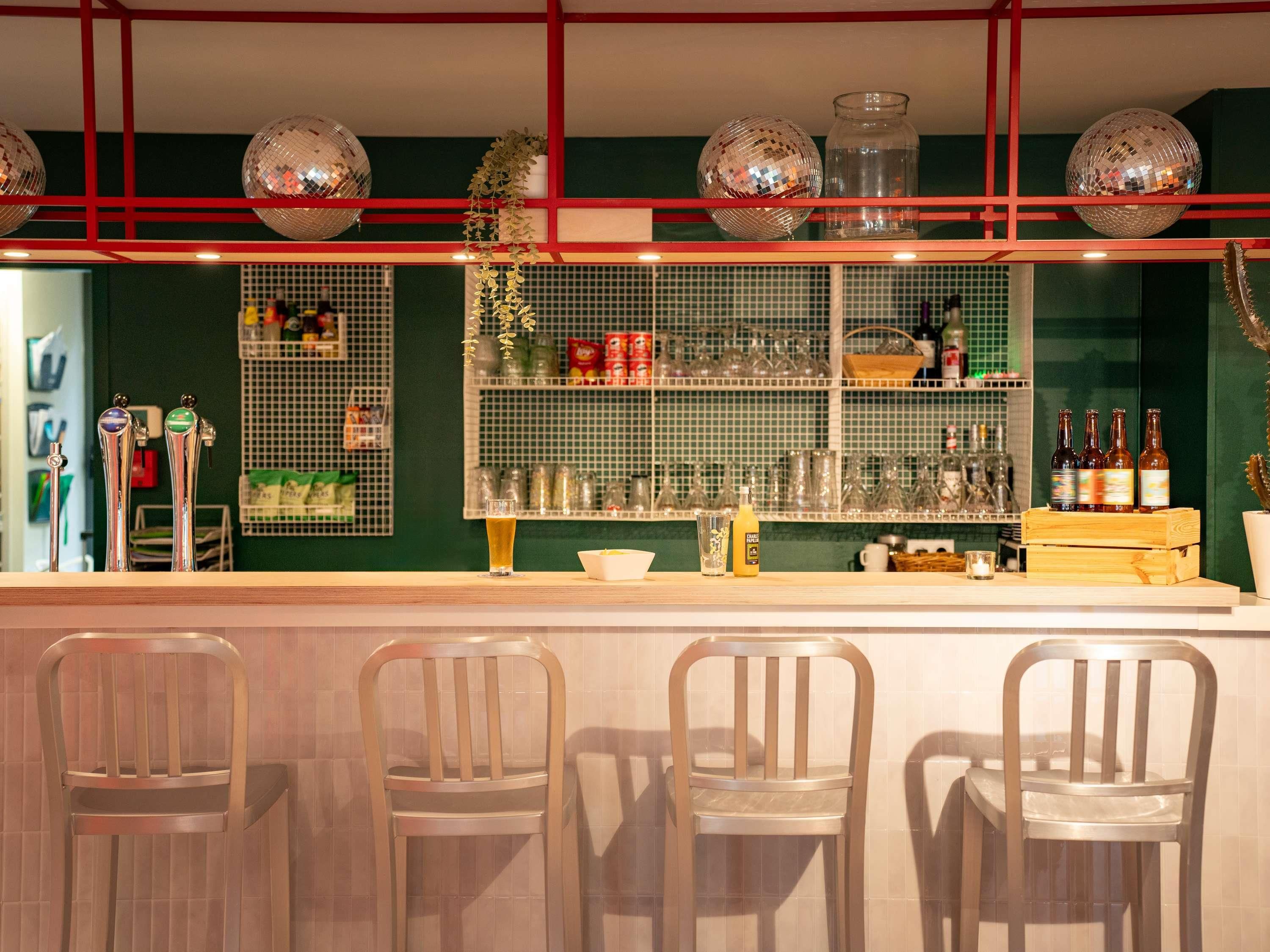 Una zona de bar con mostrador, taburetes y estantes llenos de botellas y vasos.