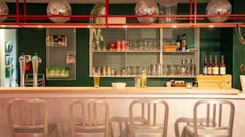 Una zona de bar con mostrador, taburetes y estantes llenos de botellas y vasos.
