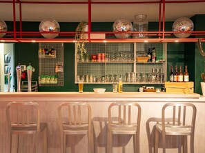 Una zona de bar con mostrador, taburetes y estantes llenos de botellas y vasos.