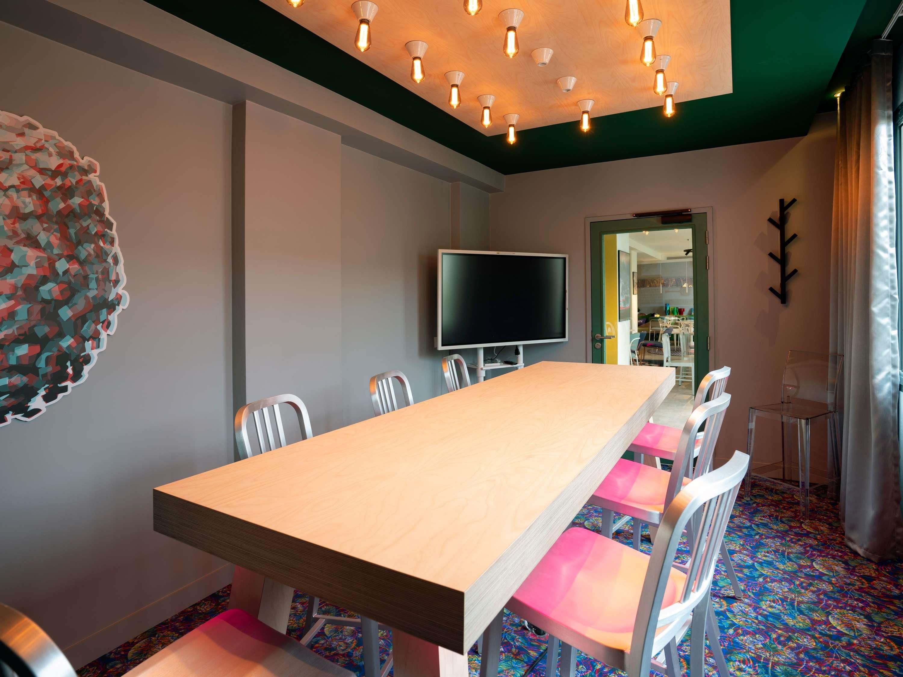 A conference room with a long table, chairs, a flat-screen TV, and a decorative wall piece.