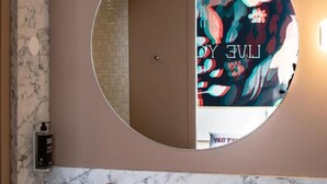 Un baño con lavamanos de mármol, un espejo redondo y un estampado de papel tapiz floral.