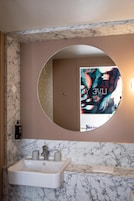 Un baño con lavamanos de mármol, un espejo redondo y un estampado de papel tapiz floral.