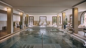 An indoor swimming pool with lounge chairs and sun loungers, surrounded by large pillars and windows. - Hotel Hacienda del Conde Meliá Collection Golf & Spa – Adults Only (Buenavista del Norte)