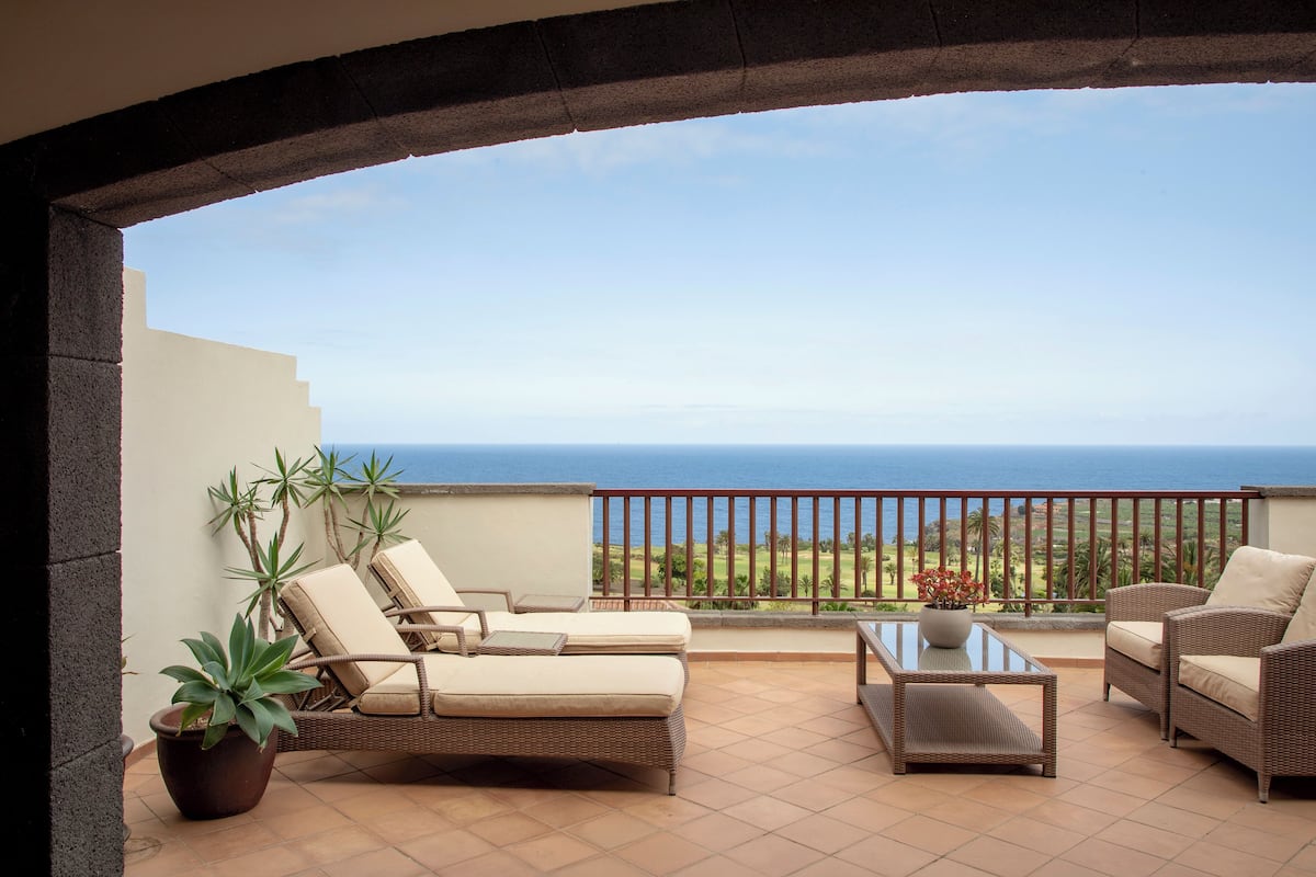 A balcony with a view of the ocean, wicker furniture, and potted plants.