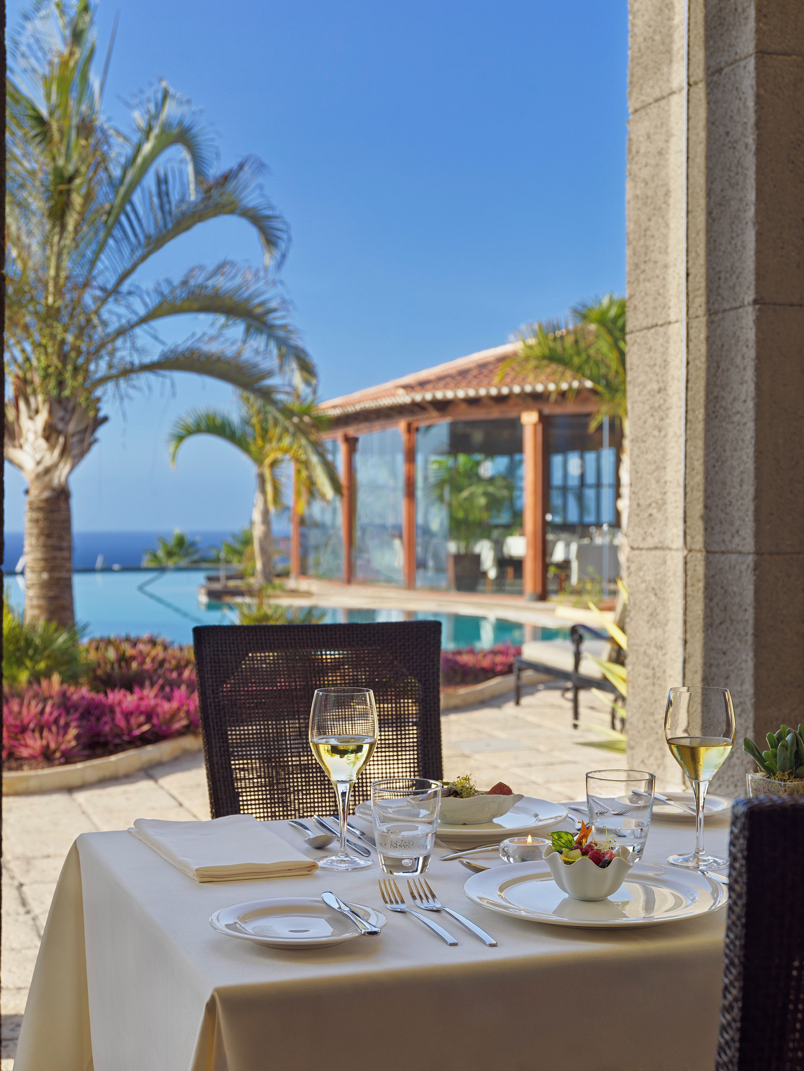 A table set for dining with a view of a pool and palm trees.