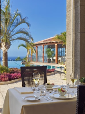 A table set for dining with a view of a pool and palm trees. - Hotel Hacienda del Conde Meliá Collection Golf & Spa – Adults Only (Buenavista del Norte)