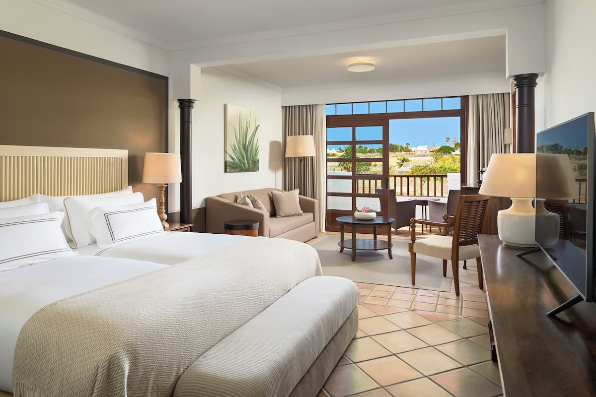 A hotel room with a large bed, a sofa, a dining table, and a TV.