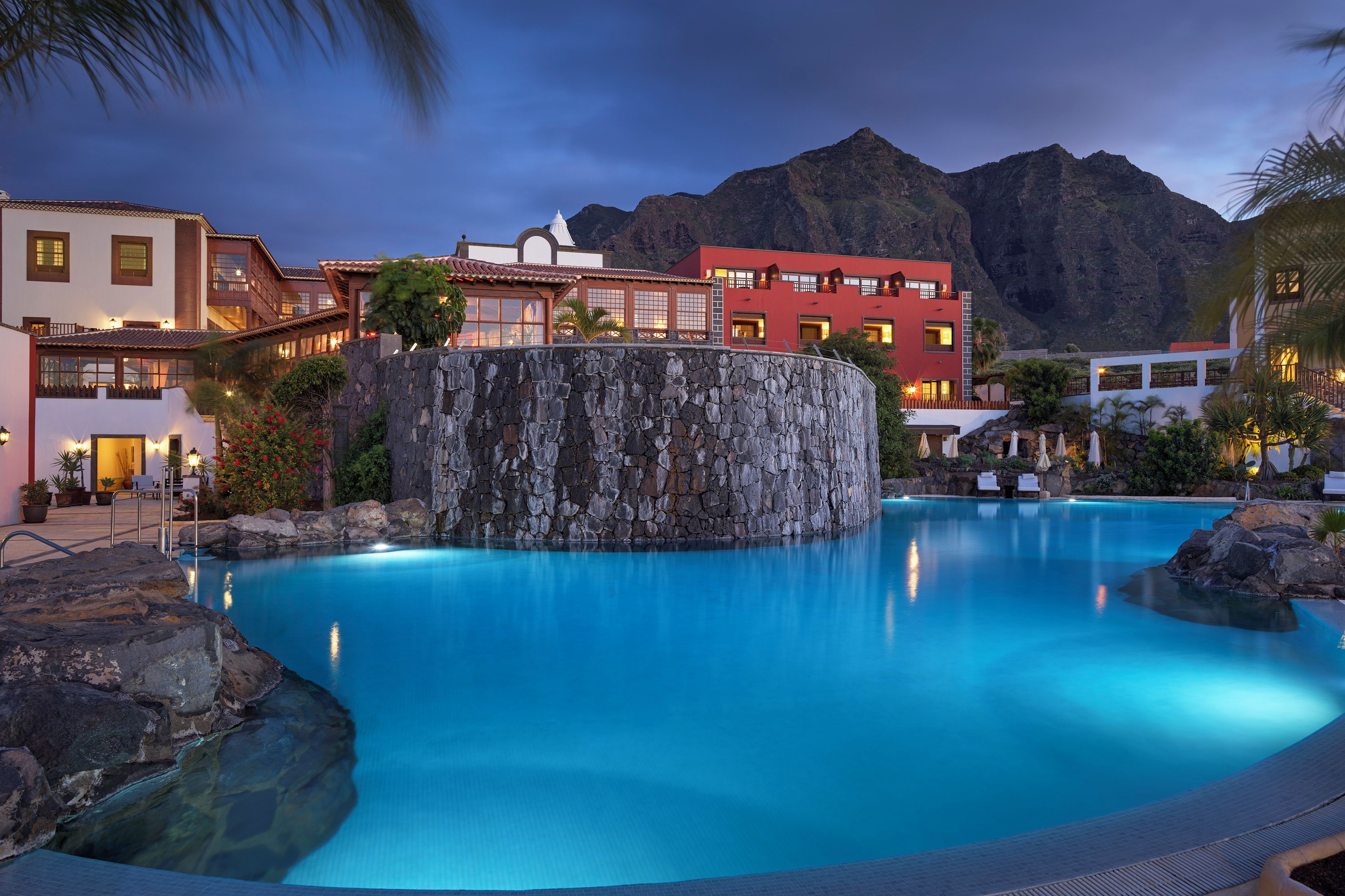 A resort with a pool, stone wall, and buildings with balconies.