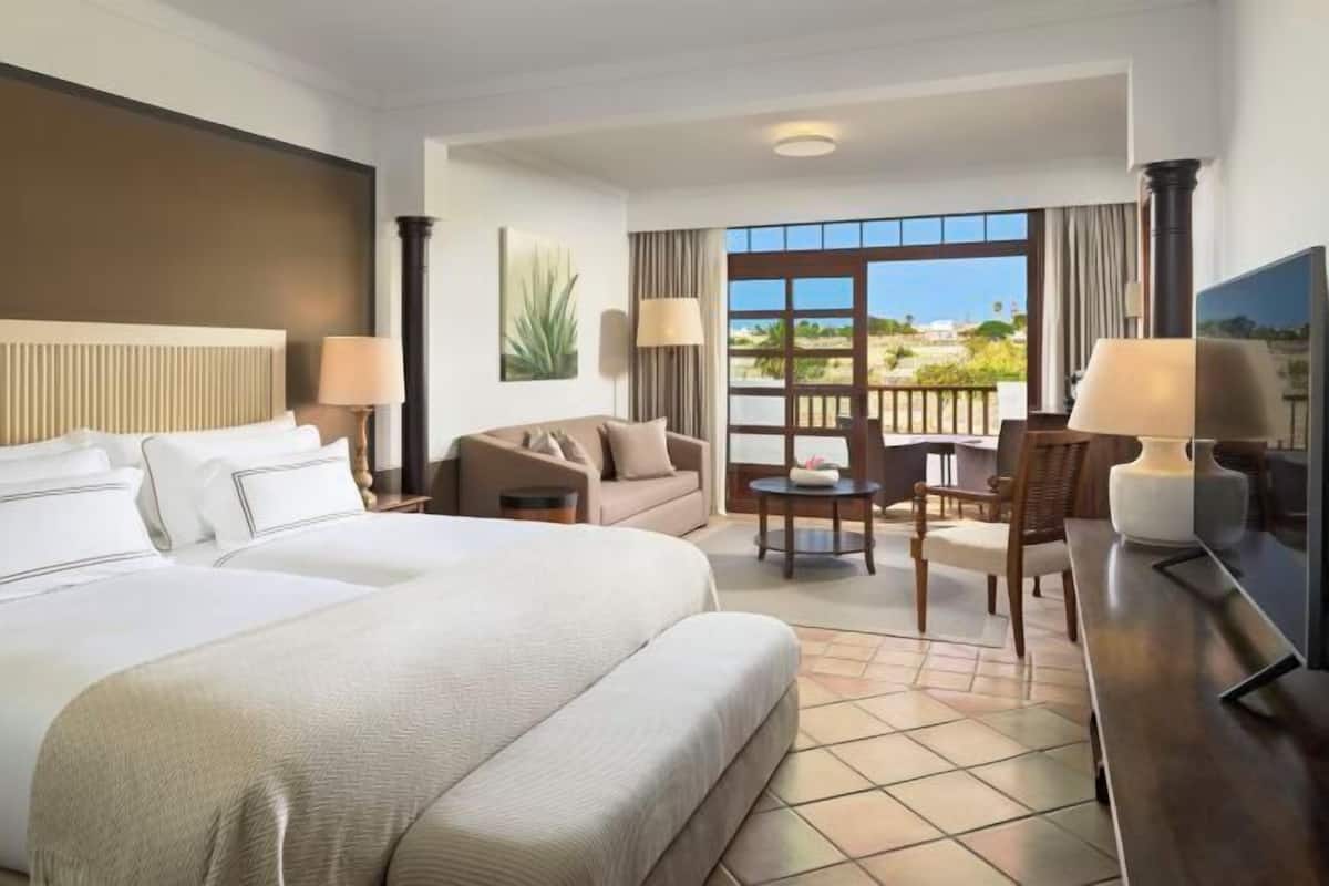 A hotel room with a large bed, a sofa, a TV, and a balcony with a view.