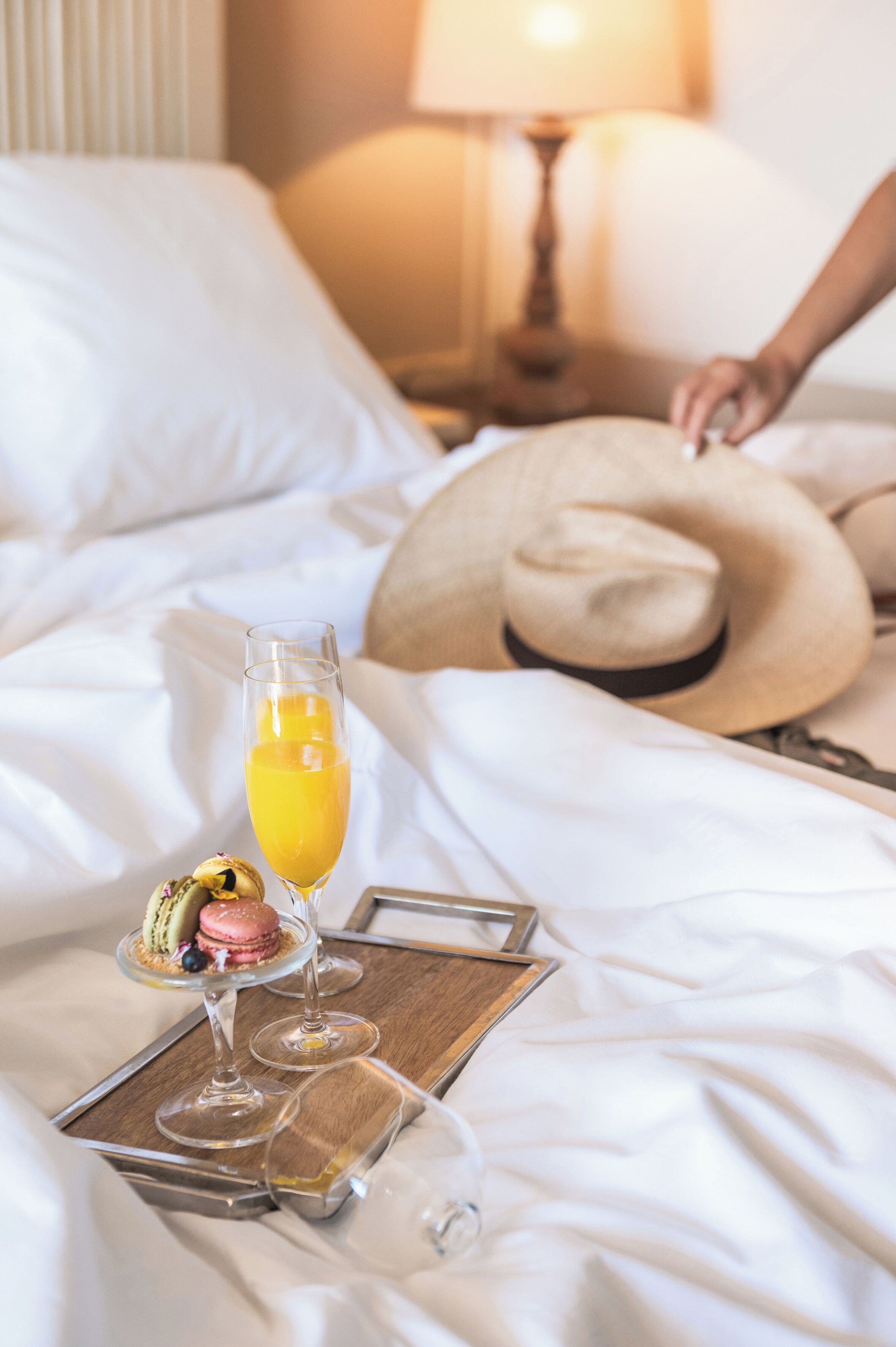 Una cama bien hecha con un vaso de zumo de naranja, un postre y una copa de vino sobre una bandeja.