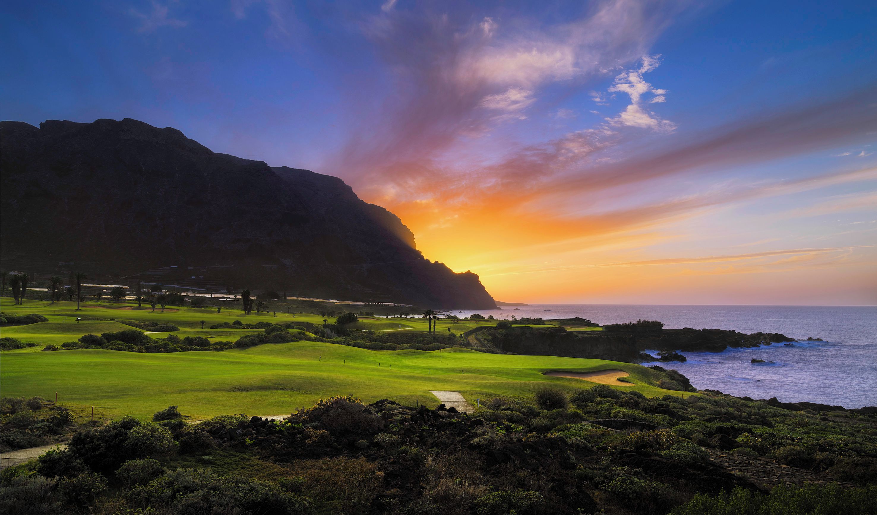 Un campo de golf frente al mar, con vista a la puesta de sol.