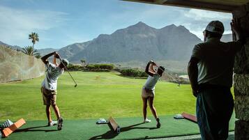 Un campo de golf con dos jugadores practicando sus golpes, un bolso de golf y un carrito de golf.