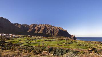 Un campo de golf costero con montañas al fondo y vista al océano.