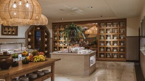 A spacious kitchen with a central island, wooden cabinets, and a variety of fruits and vegetables displayed on the counter. - Hotel Hacienda del Conde Meliá Collection Golf & Spa – Adults Only (Buenavista del Norte)