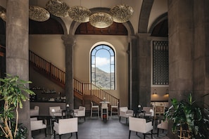 A spacious lobby with a staircase, seating area, and a large arched window overlooking a mountainous landscape. - Hotel Hacienda del Conde Meliá Collection Golf & Spa – Adults Only (Buenavista del Norte)