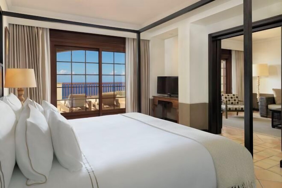 A hotel room with a large bed, a TV, a balcony with a view, and a desk.