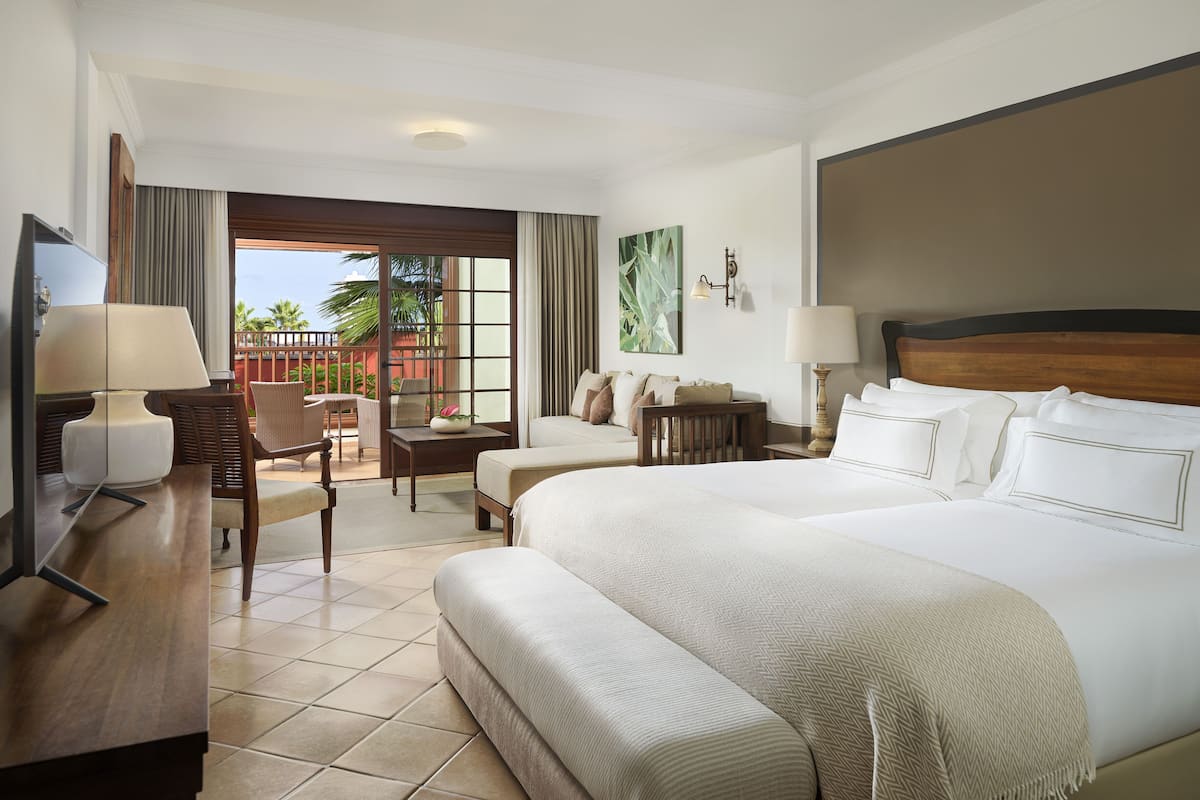 A hotel room with a large bed, a desk with a lamp, a chair, a small table, and a view of the outdoors.