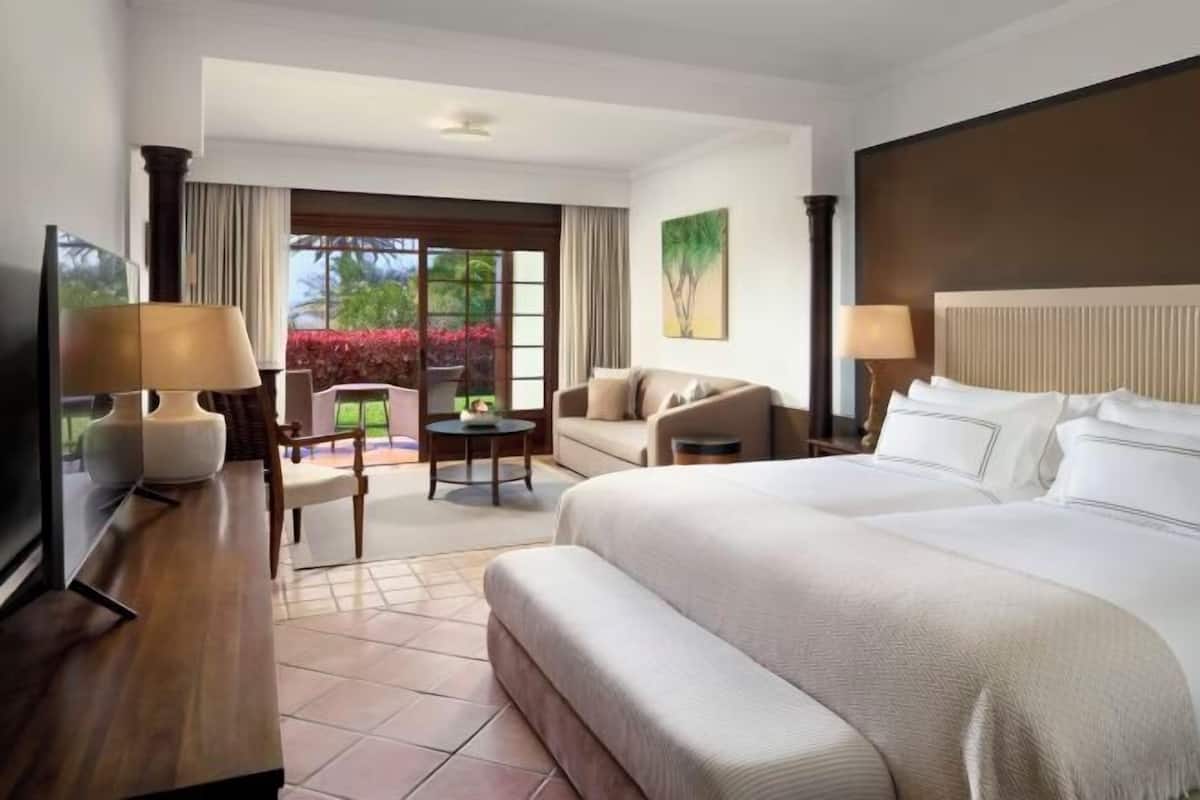 A hotel room with a large bed, a desk, a chair, a small table, and a view of the outdoors.