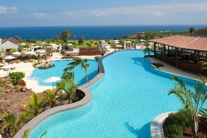 A resort pool with a curved design, surrounded by palm trees and lounge chairs, overlooking a coastal view. - Hotel Hacienda del Conde Meliá Collection Golf & Spa – Adults Only (Buenavista del Norte)