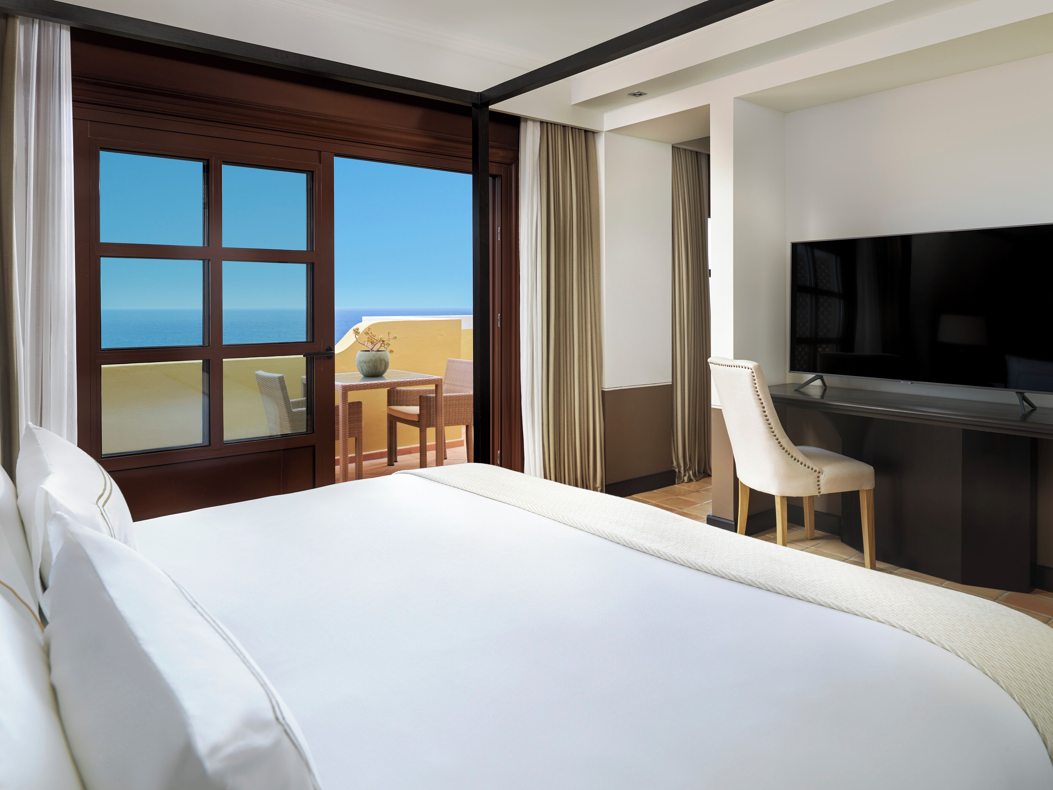 Een hotelkamer met een bed, een bureau, een stoel, een televisie en uitzicht op de oceaan.
